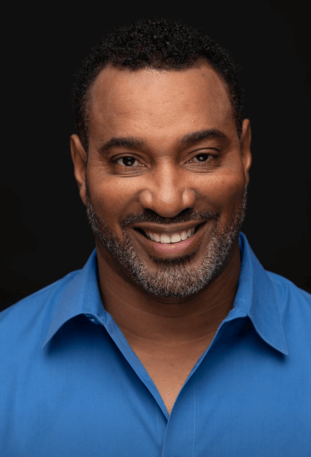 Actor John Dudley smiling in a blue shirt.