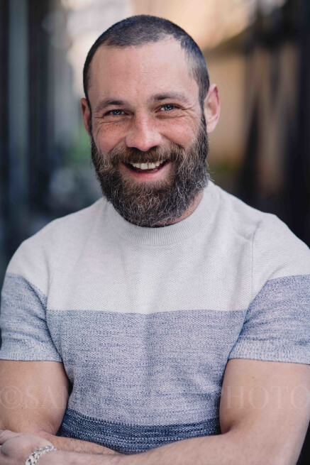 Actor Nick Sayce in a striped t-shirt smiling.