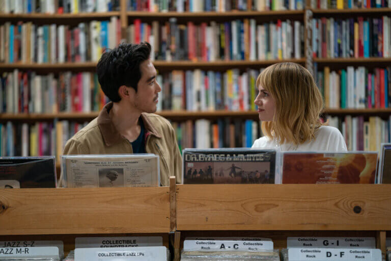 Justin H. Min and Lucy Boynton in a record store talking.