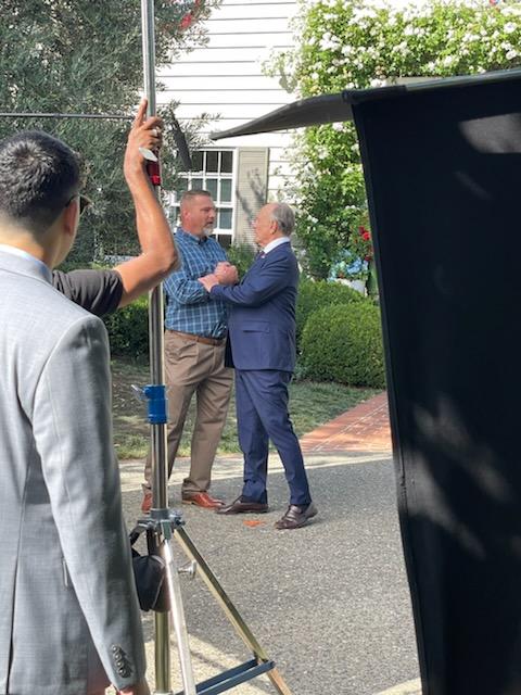 Two men embracing while filming a TV commercial outside.