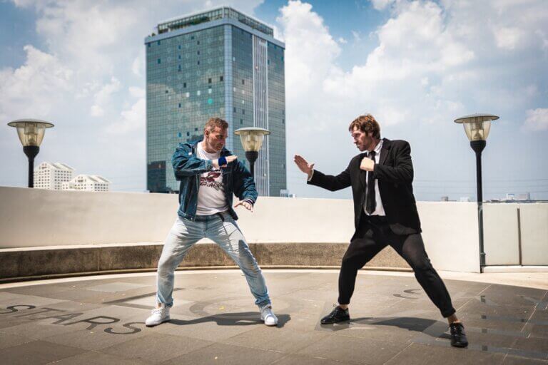 A man in street clothes in karate stance ready to fight a businessman on a roof.