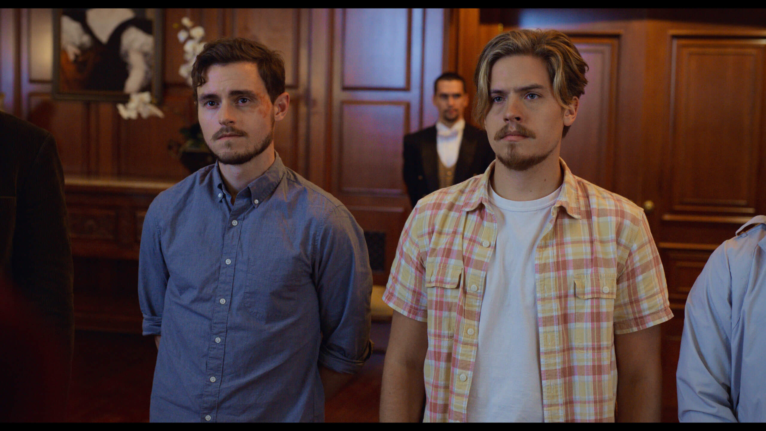 Dylan Sprouse and Callan McAuliffe looking ashamed in a courthouse.
