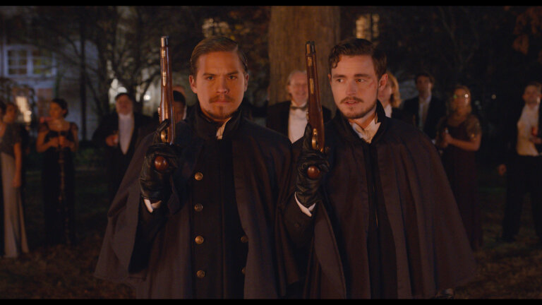 Dylan Sprouse and Callan McAuliffe in 1700s cloaks with dueling pistols.