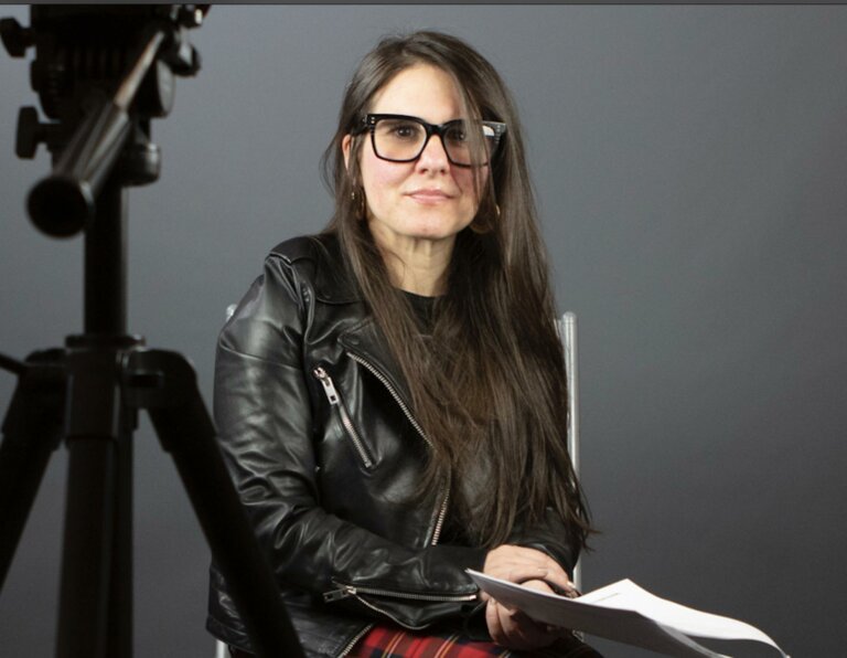 Mia Cusumano in a leather jacket smiling and sitting in a chair with a script.