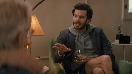Adam Brody talking to a friend on the couch inside an apartment in Netflix's 'Nobody Wants This.'
