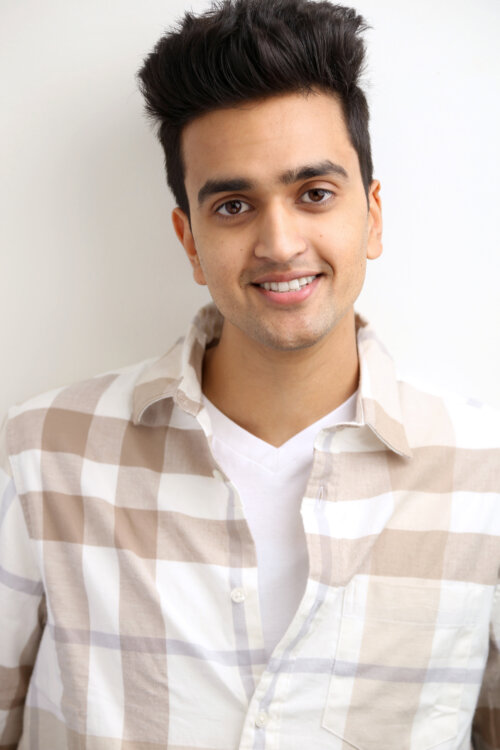 Actor Teja Chillara smiling in a white shirt with brown plaid stripes.