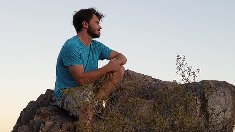 Actor Joseph Looper sitting on a rock overlooking a beautiful sunset.