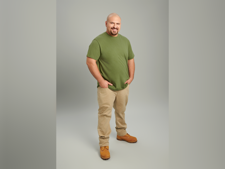 Actor Greg Hoffman smiling in a green T-shirt, tan pants and brown boots.