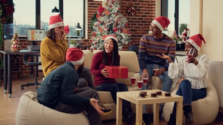Diverse group of friends exchanging holiday gifts inside.