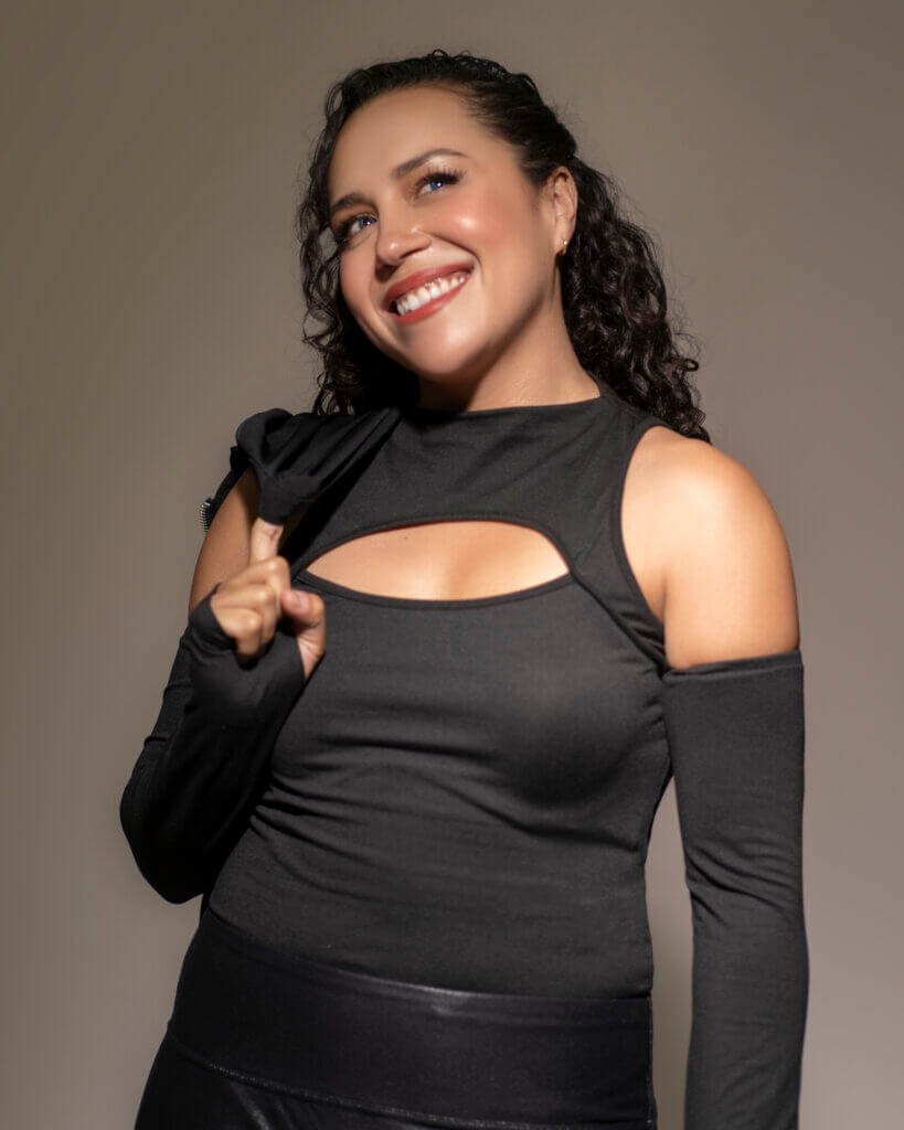 Rachel Espendez in an open black shirt smiling and raising one finger.