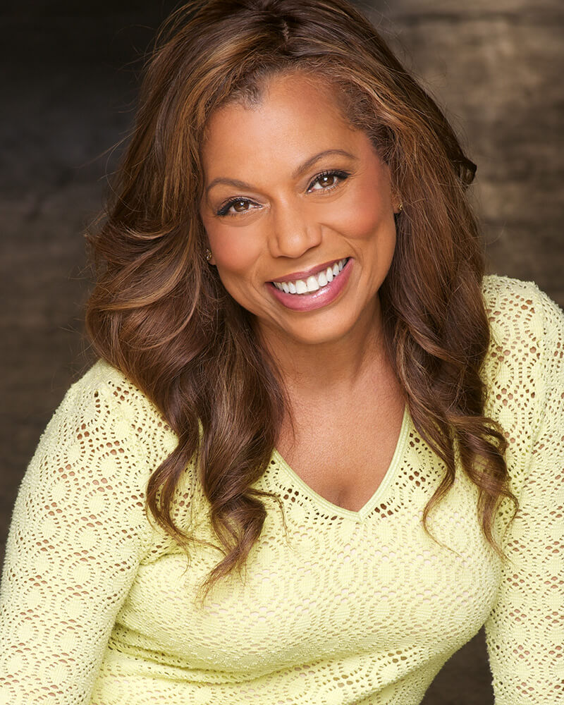 Rolonda Watts smiling in a yellow sweater inside.