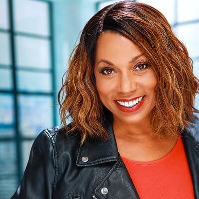 Rolanda Watts smiling in a leather jacket inside of an office building.