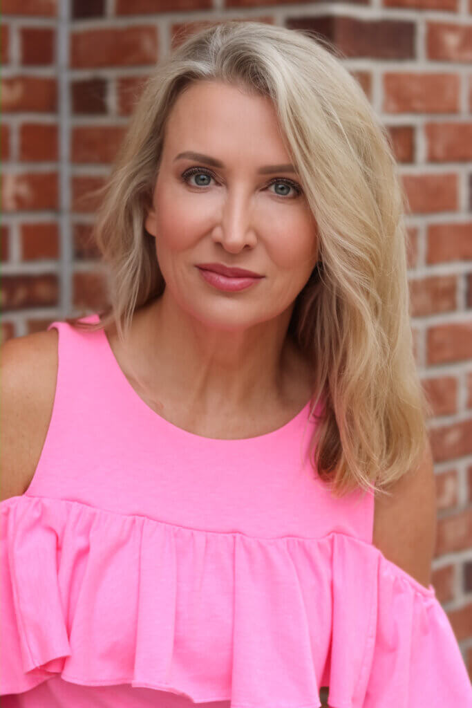 Amy McKillop smiling in front of a brick wall outside in a pink dress.