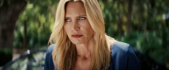 Actress Natasha Henstridge looking serious in a blue dress shirt outside by a river and trees.